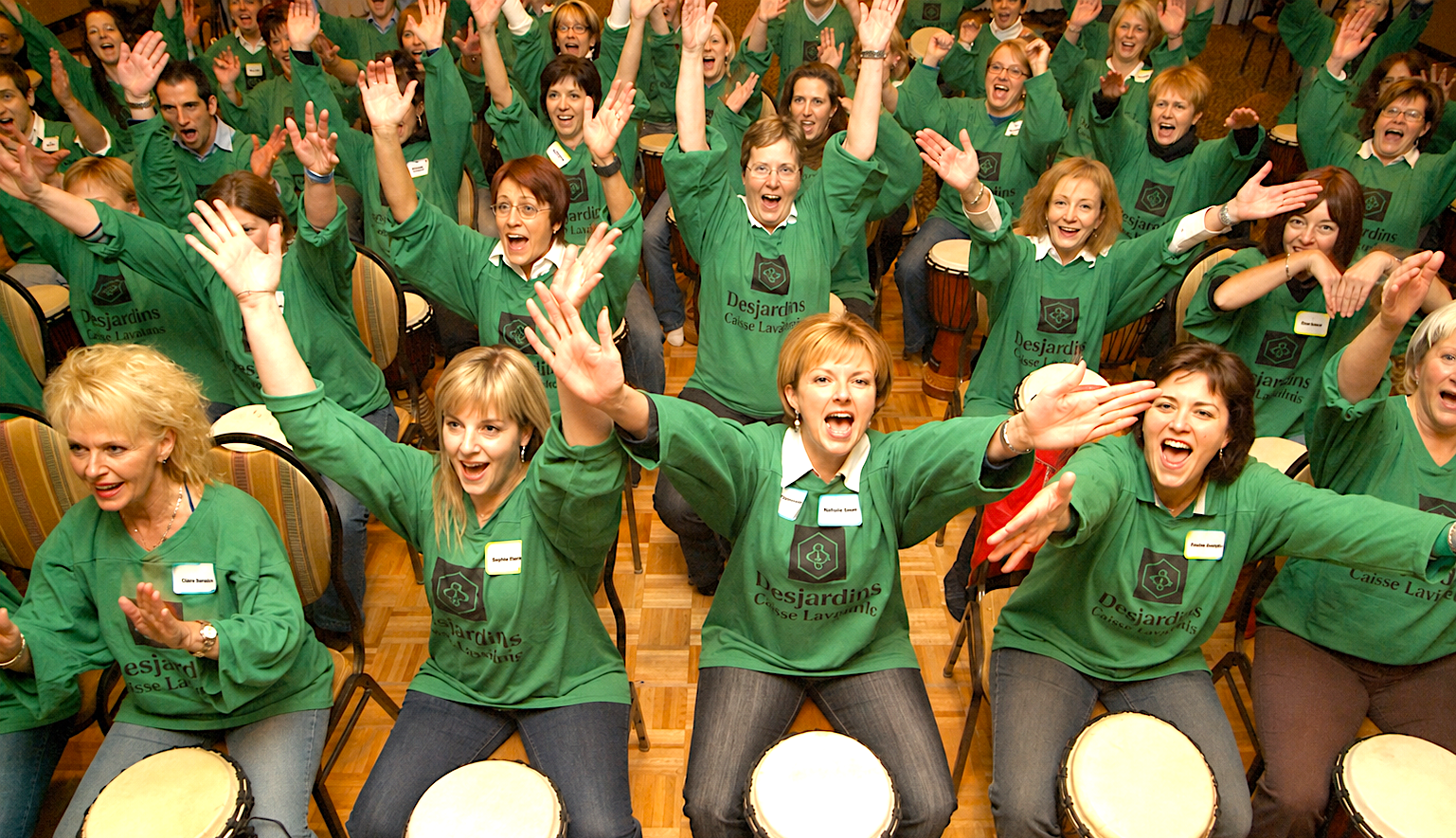 Groupe de Desjardins en chandails verts participant à un team building SAMAJAM avec des djembés.