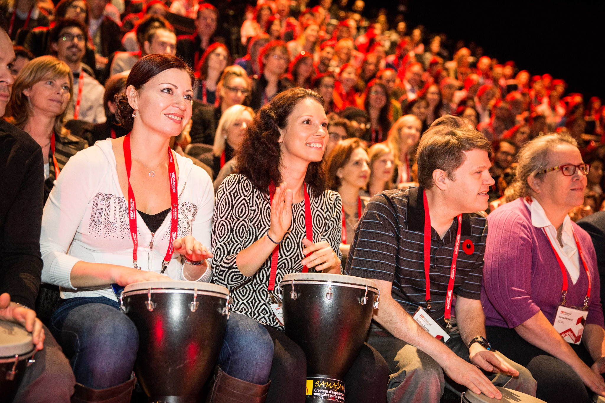 Des participants au premier rang d’un auditorium jouent du djembé. / Participants in the front row of an auditorium play djembes.